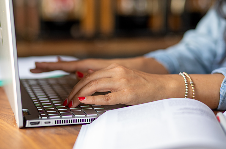 Hands with red fingernails type on a silver laptop. 